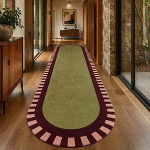 Puede incluir: Una alfombra de pasillo larga y ovalada con un centro de color verde oliva s&oacute;lido. La alfombra est&aacute; bordeada por una banda ancha de color burdeos oscuro, acentuada con un patr&oacute;n repetitivo de rayas rectangulares rosa claro en el borde exterior.