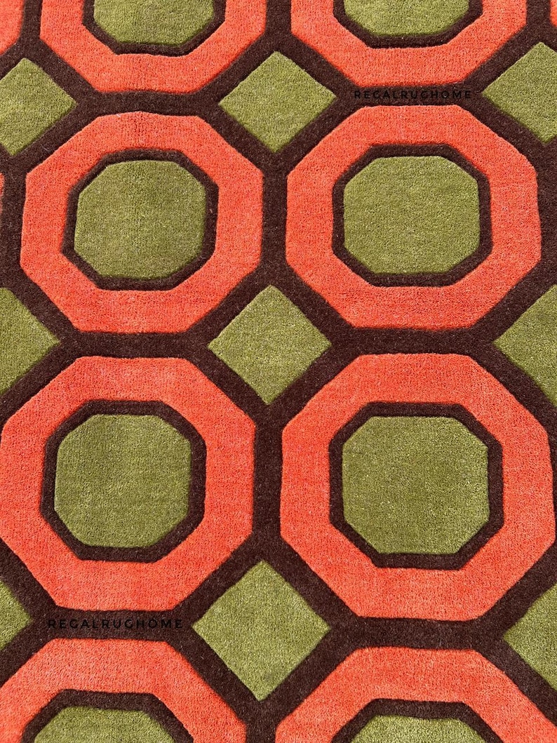 May include: A tufted rug featuring a repeating geometric pattern of orange octagons and olive green diamonds outlined in dark brown. The text REGALRUGHOME is visible in small black letters within the pattern on the rug surface.