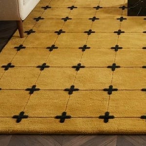 May include: A rectangular area rug featuring a solid mustard yellow background with a grid pattern formed by thin black lines. At each intersection of the grid lines, there is a small, thick black cross shape embroidered into the rug surface.