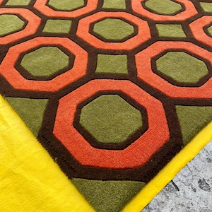 May include: A tufted area rug featuring a repeating geometric pattern of orange octagons and olive green squares separated by dark brown lines. The rug has a textured pile surface and includes the text REGALRUHOME embossed in the corner.