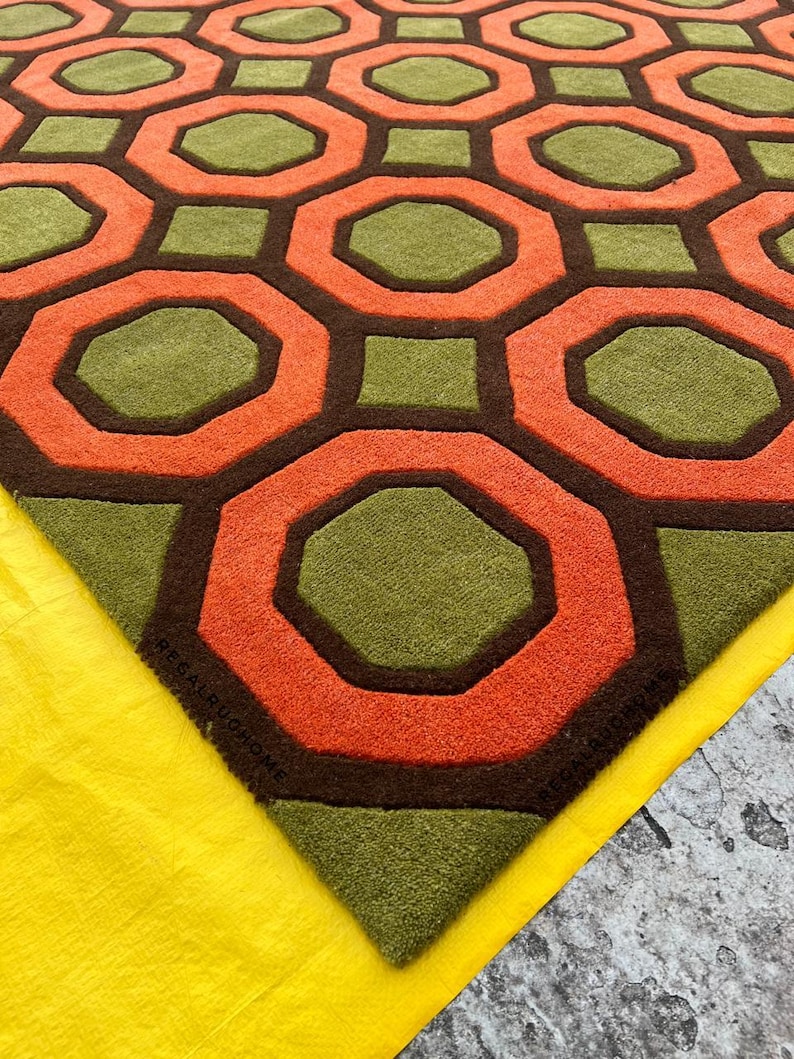 May include: A tufted area rug featuring a repeating geometric pattern of orange octagons and olive green squares separated by dark brown lines. The rug has a textured pile surface and includes the text REGALRUHOME embossed in the corner.