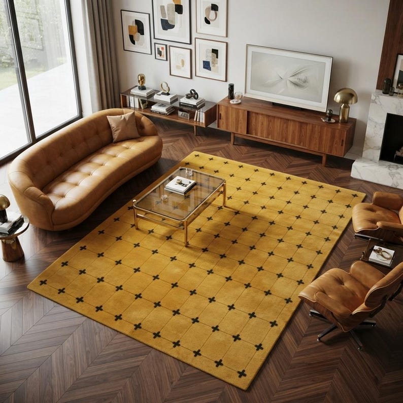May include: A large rectangular area rug featuring a mustard yellow background with a repeating grid pattern of small black cross symbols. The rug is positioned on a dark brown herringbone wood floor in a living room setting with furniture.