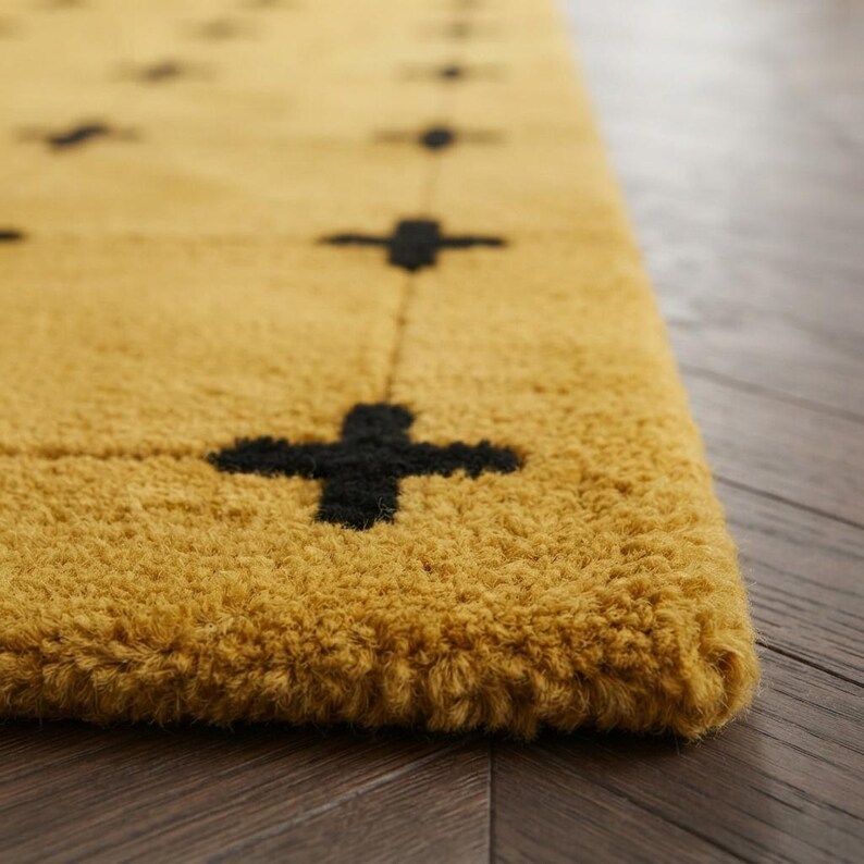 May include: A thick, mustard yellow area rug featuring a repeating grid pattern of small, dark black cross symbols. The rug has a dense, tufted pile texture and is shown at an angle, highlighting the contrast between the yellow and black colors.