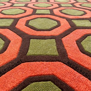 May include: A tufted area rug featuring a repeating geometric pattern of orange octagons and green squares outlined in dark brown. The text REGALRUGHOME is visible in black lettering on the orange sections of the rug surface.