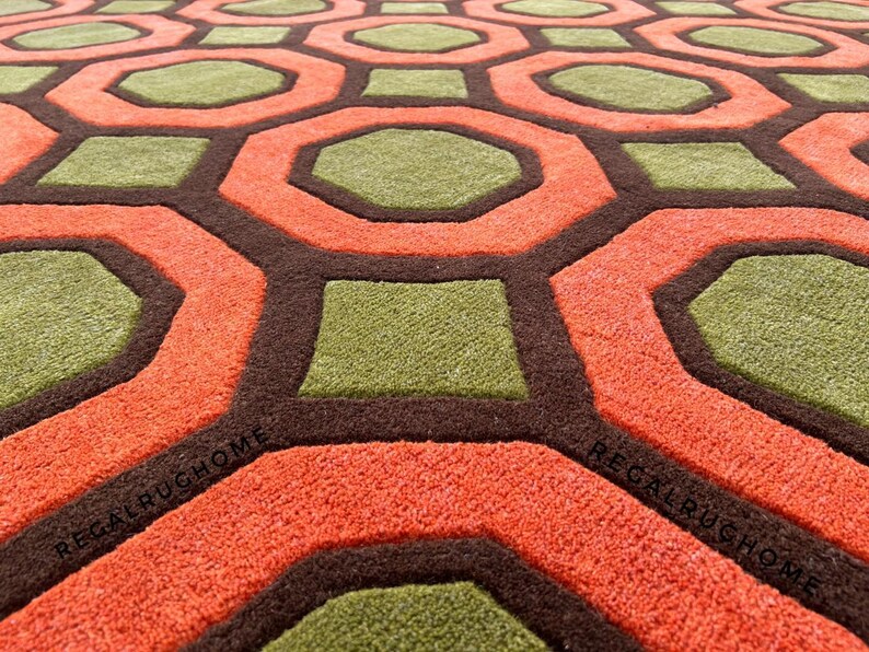 May include: A tufted area rug featuring a repeating geometric pattern of orange octagons and green squares outlined in dark brown. The text REGALRUGHOME is visible in black lettering on the orange sections of the rug surface.