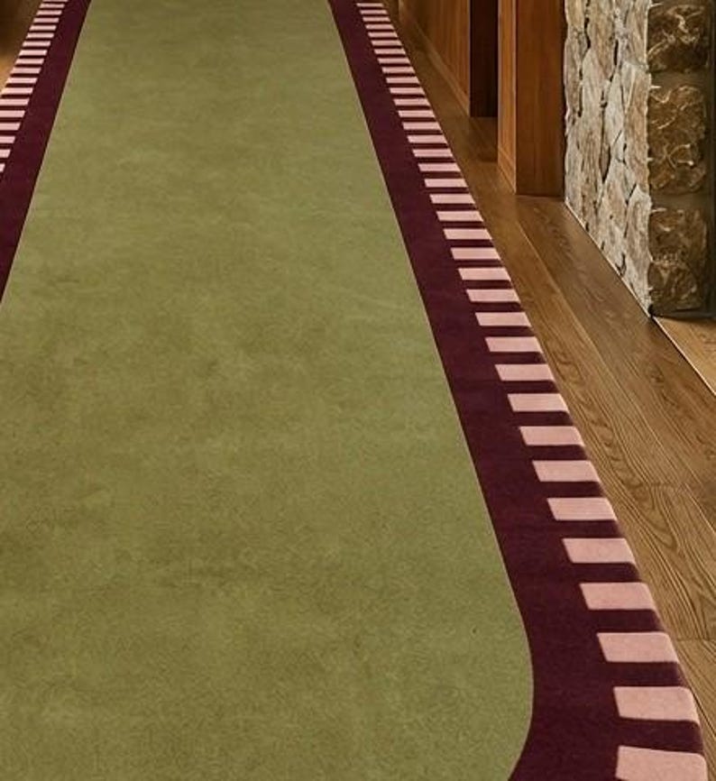 Puede incluir: Una alfombra de pasillo larga con un panel central de color verde oliva s&oacute;lido. La alfombra est&aacute; enmarcada por un borde de color burdeos oscuro acentuado con un patr&oacute;n repetitivo de bloques rectangulares de color rosa claro.