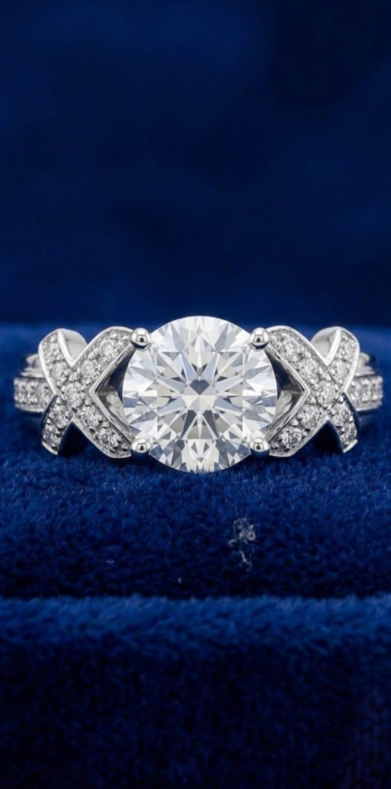 Puede incluir: Un anillo de tono plateado con una gran piedra central redonda y transparente de talla brillante, sujeta por cuatro garras. La banda est&aacute; decorada con dos motivos en forma de X a cada lado, incrustados con peque&ntilde;as piedras transparentes.