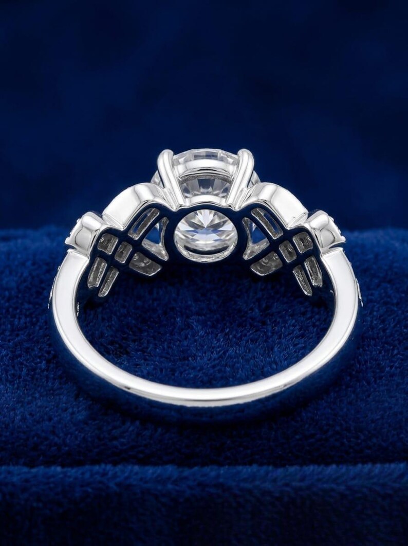 Puede incluir: Un anillo de tono plateado con una gran piedra central redonda y facetada sujeta por un engaste de m&uacute;ltiples garras. La banda presenta un dise&ntilde;o calado intrincado en ambos lados, incorporando piedras claras de corte rectangular.