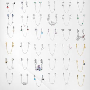 Pode incluir: Uma coleção de correntes de segurança para pulseiras de berloques prateadas e douradas, cada uma com berloques decorativos. Os berloques incluem corações, flores, animais e outros desenhos. As correntes são exibidas em um fundo branco.