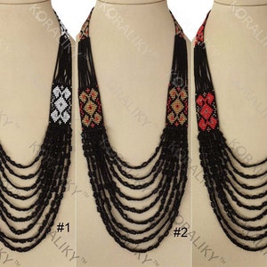 May include: Three beaded necklaces with black strands and patterned centerpieces. The first necklace has a white and black geometric design, the second has a gold, red, and black design, and the third has a red and black design.