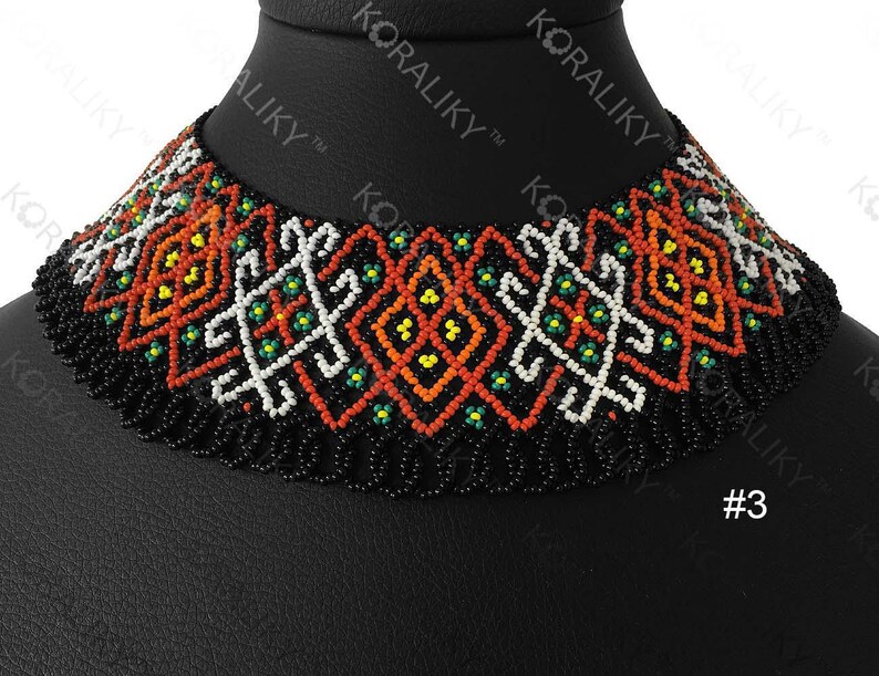 May include: A beaded choker necklace with a geometric pattern in orange, white, yellow, and green on a black background. The necklace is displayed on a black mannequin head. The word "KORALIKY" is visible.