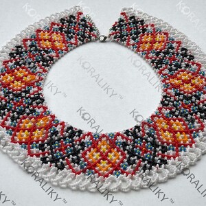 May include: A beaded necklace with a white scalloped edge. The necklace features a repeating pattern of red, orange, yellow, black, and blue beads. The text "#2" is visible on the right side of the image.