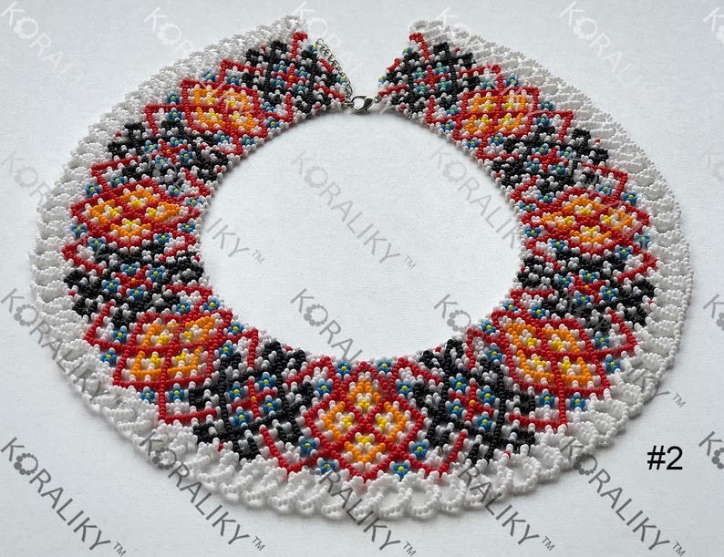 May include: A beaded necklace with a white scalloped edge. The necklace features a repeating pattern of red, orange, yellow, black, and blue beads. The text "#2" is visible on the right side of the image.