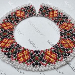 May include: A beaded necklace with a white scalloped edge. The necklace features a repeating pattern of red, orange, yellow, and black beads. The text "KORALIKY" and the number "1" are visible.