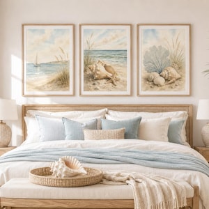 Könnte beinhalten: Ein Set aus drei gerahmten Wandbildern im Aquarellstil, die Küstenszenen mit einem Segelboot, Muscheln und Korallen zeigen. Die Kunstwerke in hellen Holzrahmen weisen sanfte Blau-, Beige- und Weißtöne auf und hängen über einem Bett mit neutraler Bettwäsche.