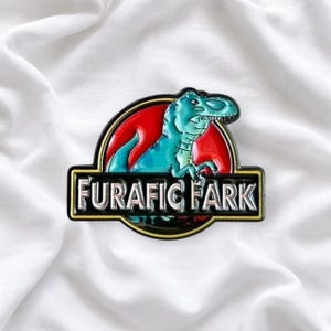 May include: A circular enamel pin featuring a teal dinosaur silhouette against a red background, enclosed in a black border. A horizontal black bar across the center displays the silver metallic text FURAFIC FARK in a bold, capitalized font.
