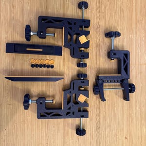 Puede incluir: Un conjunto de abrazaderas y accesorios para carpintería en negro y naranja, que incluye varias abrazaderas en C, una abrazadera larga y pequeñas piezas circulares naranjas. Las abrazaderas tienen tornillos ajustables.
