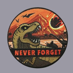 May include: Embroidered patch featuring a Tyrannosaurus Rex with an open mouth, set against a fiery orange and red sunset backdrop. The patch includes the text "NEVER FORGET" in red, with silhouettes of flying creatures and a volcano.
