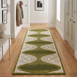 May include: A long rectangular runner rug featuring a repeating pattern of olive green oval shapes and beige sections with concentric line details. The rug is centred on a light-coloured wooden floor in a hallway, showcasing a geometric design.