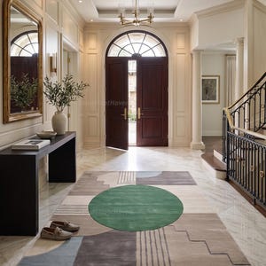 May include: A rectangular area rug featuring a large central green circle surrounded by geometric shapes in shades of beige, gray, and light blue. The design includes stepped patterns and parallel lines, laid out on a polished marble floor in a foyer.