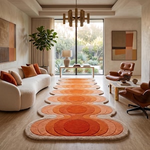 Peut inclure: Un long tapis de type chemin présentant un motif répétitif de cercles concentriques dans des tons orange, orange brûlé et crème. Le tapis possède une forme de bordure organique et ondulée qui suit le design circulaire sur un sol en pierre.