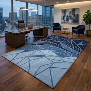 May include: A large rectangular area rug featuring a geometric pattern of intersecting lines in various shades of blue, ranging from light sky blue to deep navy. The rug is placed on a dark brown hardwood floor in a modern office setting.