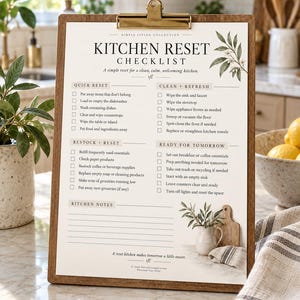 Pode incluir: Uma prancheta de madeira com uma lista de verificação impressa Kitchen Reset, contendo seções para limpeza, organização e preparação. O papel apresenta ilustrações botânicas e um espaço reservado para notas de cozinha.