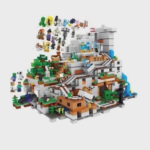 Könnte beinhalten: Ein mehrstöckiges Baustein-Set, das eine Berglandschaft mit grauen Stein-, grünen Gras- und braunen Erdblöcken darstellt. Die Struktur umfasst eine Lorenschiene, verschiedene kleine Spielfiguren und aus Bausteinen gefertigte Bäume.
