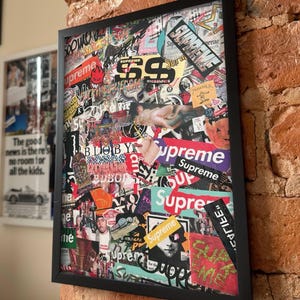 Peut inclure: Une &oelig;uvre d'art murale rectangulaire dans un cadre noir pr&eacute;sentant un collage dense de divers autocollants et impressions graphiques. La composition comprend plusieurs occurrences du mot Supreme dans diff&eacute;rentes polices et couleurs, ainsi que divers motifs.