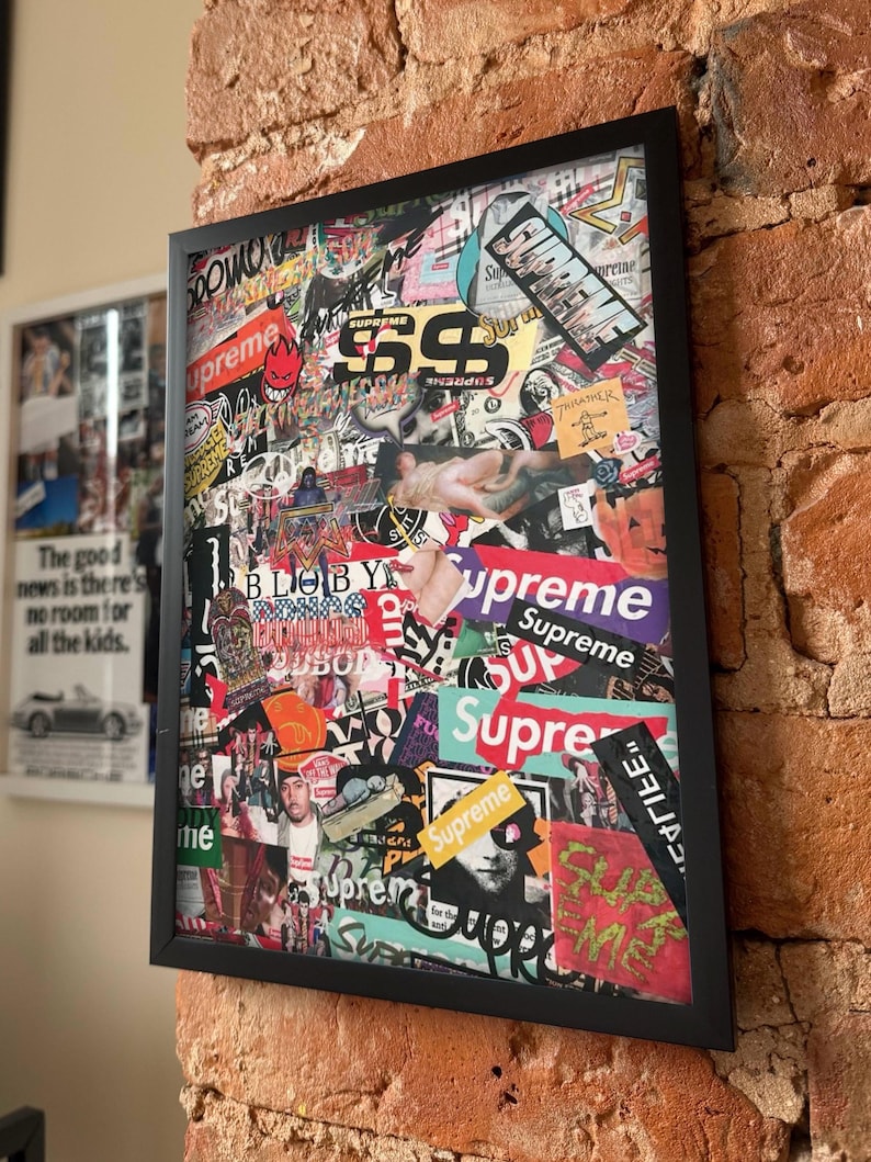 Peut inclure: Une &oelig;uvre d'art murale rectangulaire dans un cadre noir pr&eacute;sentant un collage dense de divers autocollants et impressions graphiques. La composition comprend plusieurs occurrences du mot Supreme dans diff&eacute;rentes polices et couleurs, ainsi que divers motifs.