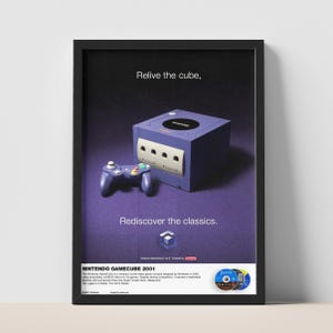 Può includere: Un poster incorniciato con una console Nintendo GameCube viola e il controller abbinato. Il testo recita Relive the cube, Rediscover the classics e NINTENDO GAMECUBE 2001, con una descrizione della console e tre piccoli dischi di gioco.