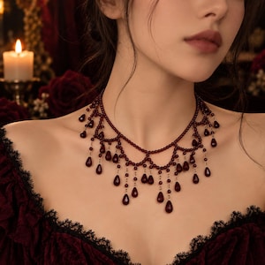 May include: A multi-layered necklace featuring deep red, round beads arranged in a scalloped pattern. Numerous teardrop-shaped red beads hang from the base of the scalloped strands, creating a fringe effect that rests against the collarbone area.
