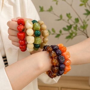 May include: Several colorful beaded bracelets. One bracelet features red, white, green, and tan beads. Another bracelet has brown, purple, and orange beads. The bracelets are made of large, irregular shaped beads.