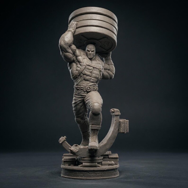 May include: A gray statue of a muscular figure wearing a mask and lifting a stack of weight plates overhead. The figure is posed on a circular base with a stylized support structure. The statue is detailed and appears to be made of a solid material.