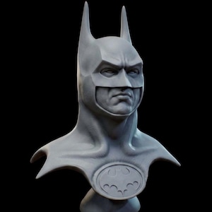 Könnte beinhalten: Graue Batman-Büste, die die Maske der Figur mit spitzen Ohren und einem ernsten Gesichtsausdruck zeigt. Auf der Brust ist das ikonische Fledermaussymbol zu sehen. Die Skulptur ist vor einem schwarzen Hintergrund platziert.