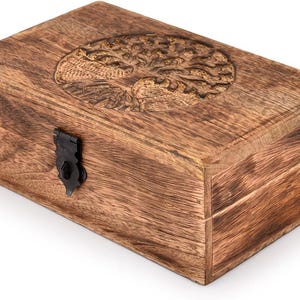 Puede incluir: Una caja rectangular de madera con un diseño de árbol de la vida tallado en la tapa. La caja es de madera marrón claro y tiene un cierre de metal negro. Se aprecia la veta de la madera.