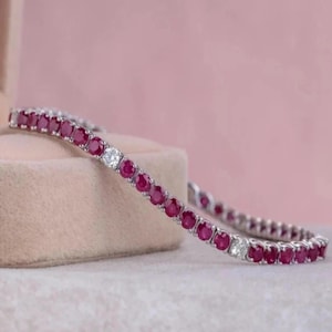 May include: A tennis bracelet featuring a continuous row of round, deep red rubies set in a metallic band, accented by occasional clear, round-cut stones spaced evenly throughout the design to create a repeating pattern of red and white.