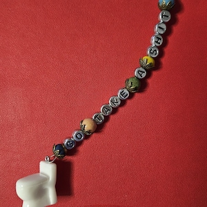 May include: A novelty beaded keychain with the phrase "GO TAKE A SHIT" spelled out in silver letter beads. The keychain features a small white toilet charm and colorful decorative beads against a red background.