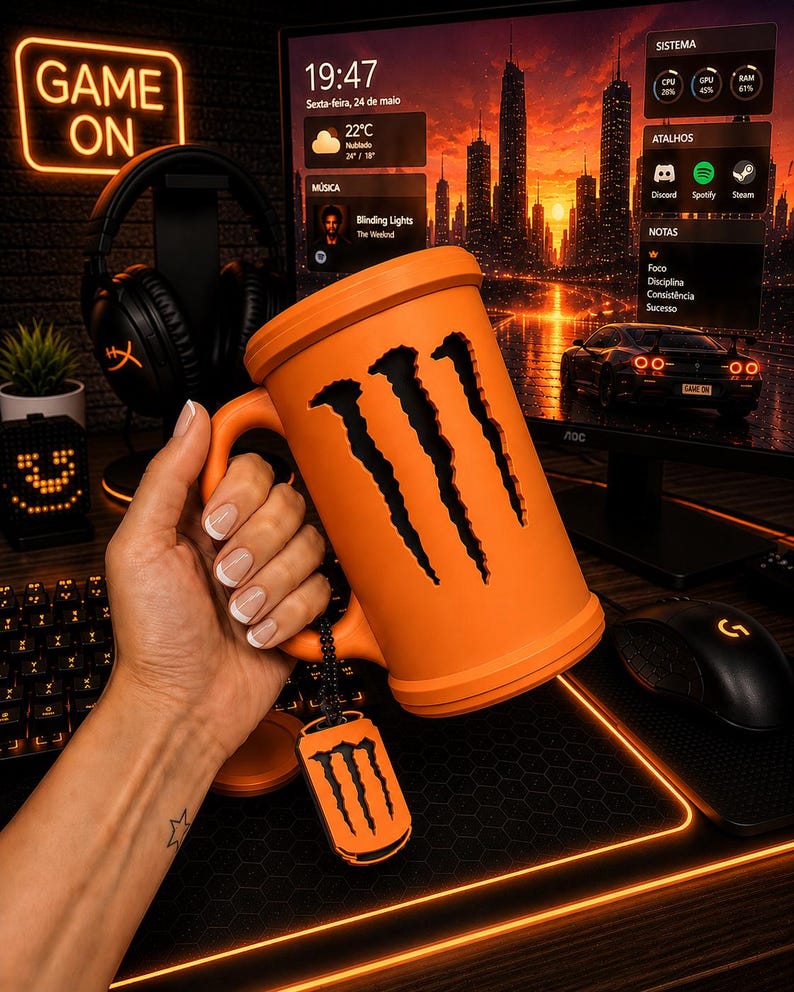 May include: A bright orange mug featuring a cutout of the three-claw Monster Energy logo on its side. The mug includes a matching orange lid and a small, dangling orange dog tag-style charm that also displays the black three-claw logo.