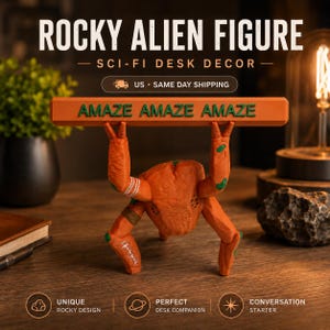 May include: An orange alien figure with a textured surface, featuring green accents and white markings on its limbs. The figure is positioned in a crouched stance, holding a long, horizontal orange bar above its head with the text AMAZE AMAZE AMAZE.