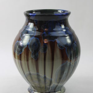 May include: A ceramic vase with a dark brown and blue glaze. The vase has a round body and a narrow neck. The glaze has a streaky effect, with shades of brown, blue, and white.