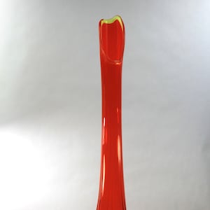 May include: A tall, red glass vase with a flared opening and a three-legged base. The vase has a slight yellow tint at the base.