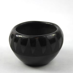 May include: A black pottery bowl with a geometric design. The bowl is round and has a wide opening. The design is made up of triangles that are arranged in a repeating pattern.