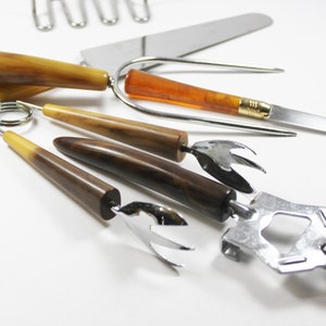 May include: A set of vintage kitchen tools with brown, amber, and yellow bakelite handles. The tools include a bottle opener, a cheese knife, a fork, and a pair of tongs.