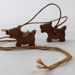 May include: Two wooden dog charms on a brown cord. The dogs are brown and have a simple design.