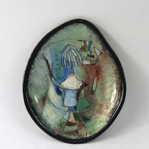 May include: A ceramic plate with a black rim and a colorful abstract design featuring a stylized figure and birds. The design is painted in shades of blue, green, red, and white.