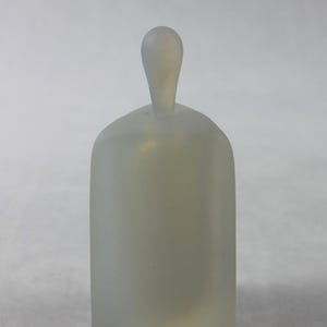May include: A frosted glass bottle with a rounded top and a rectangular body. The bottle is opaque and has a milky white color.