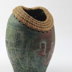 May include: A ceramic vase with a woven rim, featuring a green and red abstract design.