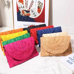 Könnte beinhalten: Eine Auswahl an farbenfrohen gewebten Clutch-Geldbörsen in verschiedenen Farbtönen, darunter Pink, Orange, Gelb, Grün, Rot, Schwarz, Blau und Naturbeige. Jede Geldbörse hat einen Klappenverschluss und eine gewebte Textur, ideal für Essentials.