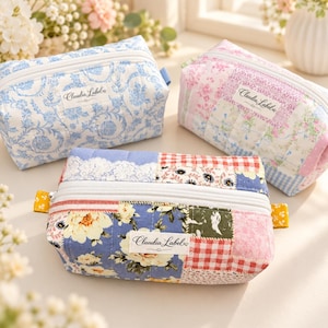 May include: Three rectangular quilted pouches with white zippers and a Claudia Label tag. One features a blue and white floral pattern, another a pink and white floral patchwork, and the third a multi-colored floral and gingham patchwork design.